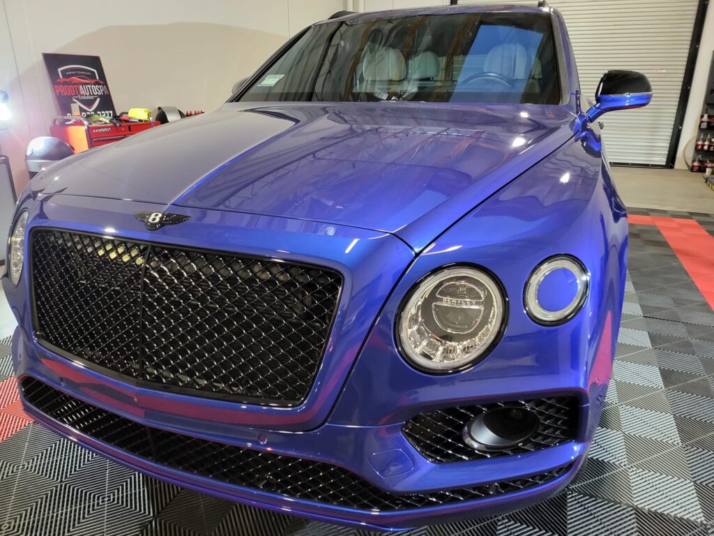 Shiny blue Bentley parked in garage with checkered floor.